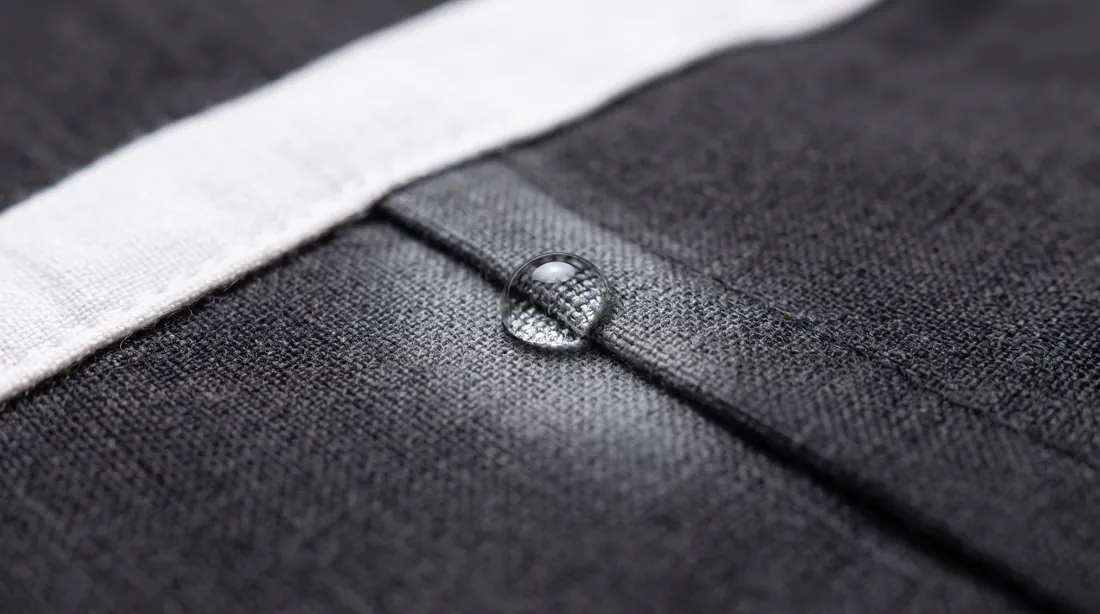 Single drop of liquid sitting on dark fabric near a seam with white trim