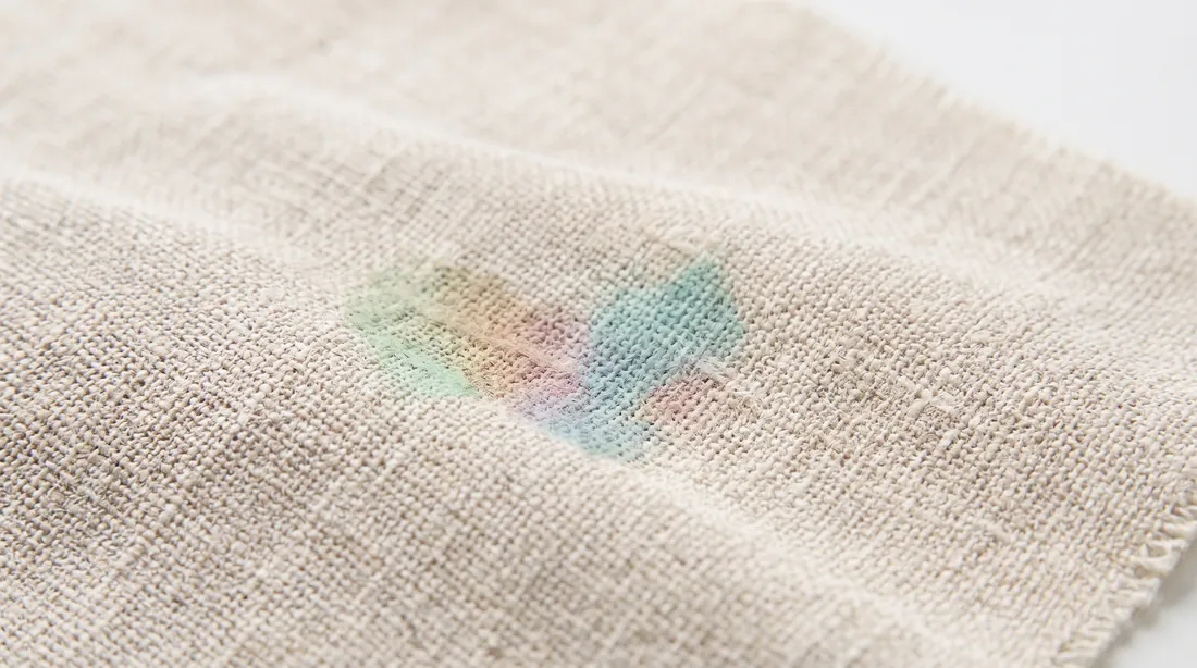 Faint multicoloured stain on beige linen below a row of printed care symbols