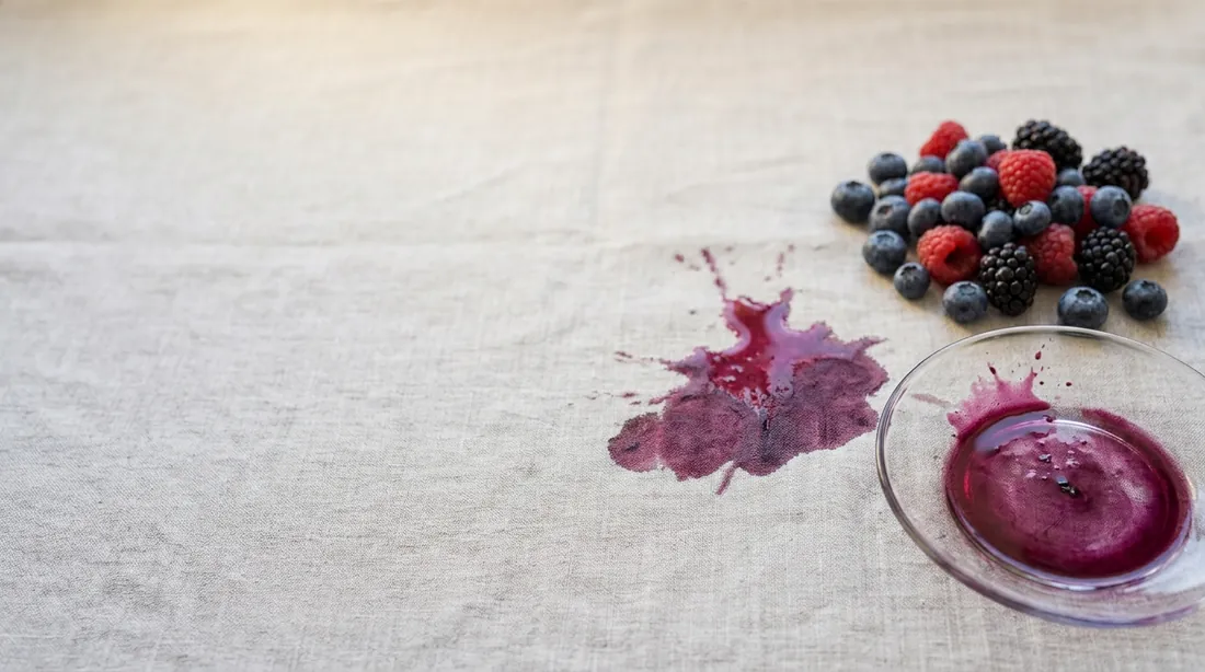 Berry juice stain beside a bowl of mixed berries on linen