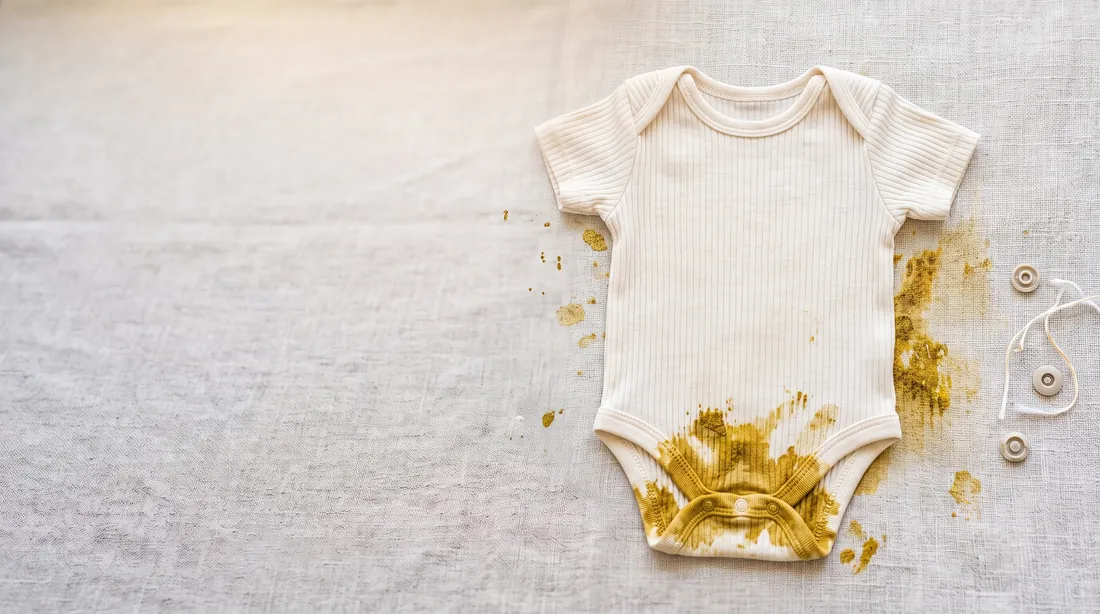 Yellow-brown feces stain on a white baby bodysuit on linen