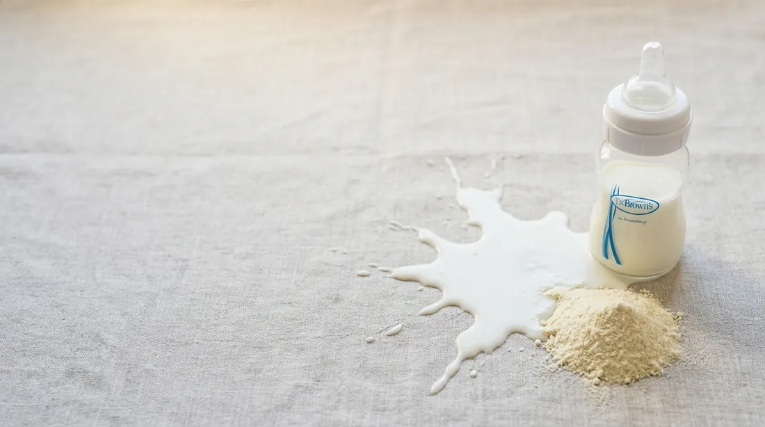 Spilled milk and formula powder beside a baby bottle on linen