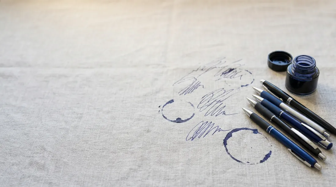 Ballpoint pens and an ink bottle with ink marks and rings on linen