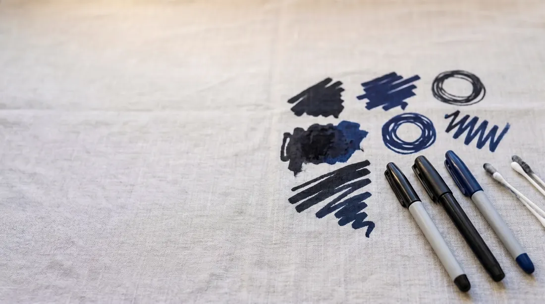 Dark permanent marker scribbles on linen with markers laid beside them