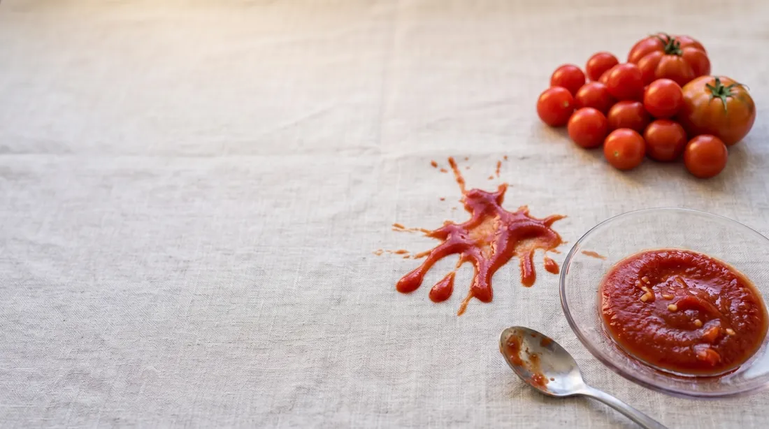 Ketchup and tomato sauce spilled on linen beside a bowl of tomatoes